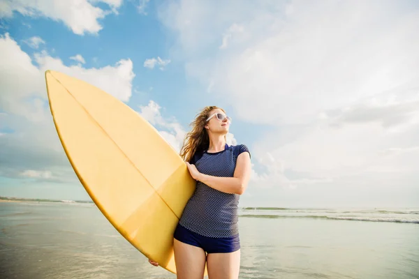 Beautiful young caucasian girl in rushwest and sunglasses with yellow surfboard at legian beach, Bali. Lyfestyle, leisure, sport, vacation, happines concept — Stock Photo, Image