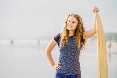 güzel genç sörfçü kız sarı surfboard ile gün batımında sahilde kalıyor. sağlıklı yaşam tarzı, boş zaman, seyahat, tatil ve spor kavramı, boşaltmak