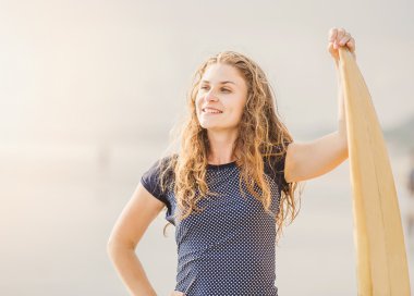 güzel genç sörfçü kız sarı surfboard ile gün batımında sahilde kalıyor. sağlıklı yaşam tarzı, boş zaman, seyahat, tatil ve spor kavramı, boşaltmak