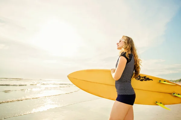 Beautiful young caucasian girl in rushwest and sunglasses with yellow surfboard at legian beach, Bali. Lyfestyle, leisure, sport, vacation, happines concept — Stock Photo, Image