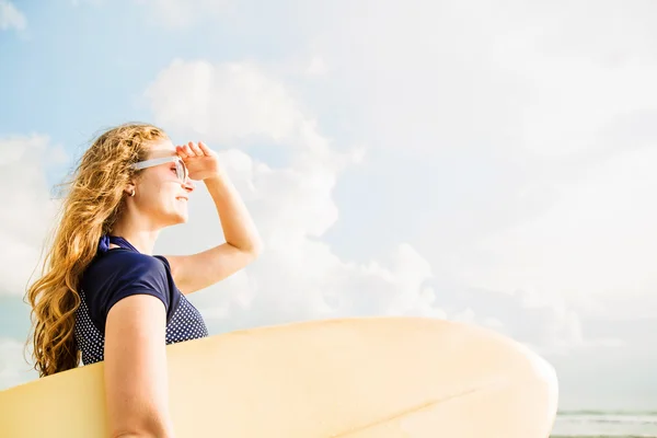 Piękna młoda dziewczynka kaukaski w rushwest i okulary z żółtym surfingowej na plaży legian bali. lyfestyle, wypoczynek, sport, wakacje, pojęcie szczęścia — Zdjęcie stockowe