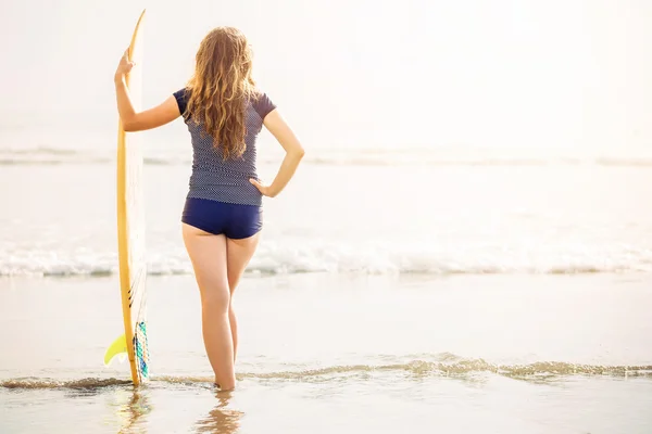 Beautiful young surfer girl stays on the beach at sunset with yellow surfboard. Healthy lifestyle, leisure, travel, holiday and sport concept, copyspace — Stock Photo, Image
