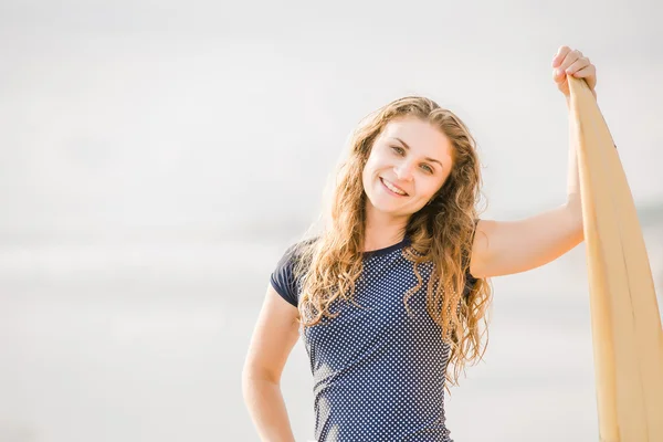 Beautiful young surfer girl stays on the beach at sunset with yellow surfboard. Healthy lifestyle, leisure, travel, holiday and sport concept, copyspace — Stock Photo, Image