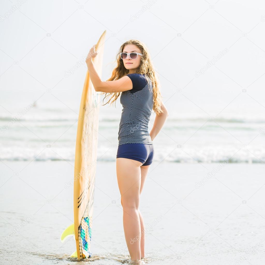 Beautiful young surfer girl stays on the beach at sunset with yellow surfboard. Healthy lifestyle, leisure, travel, holiday and sport concept, copyspace