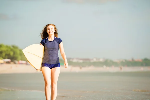 Όμορφη σέξι surfer κορίτσι στην παραλία στο ηλιοβασίλεμα περιπάτους κατά μήκος του ωκεανού ακτή, κίτρινο σανίδα του σερφ στα χέρια της. υγιή ζωή, έννοια άθλημα με copyspace — Φωτογραφία Αρχείου