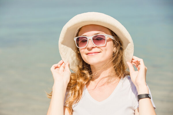 Яркий портрет привлекательной молодой женщины в солнечных очках на пляже, загорающей
