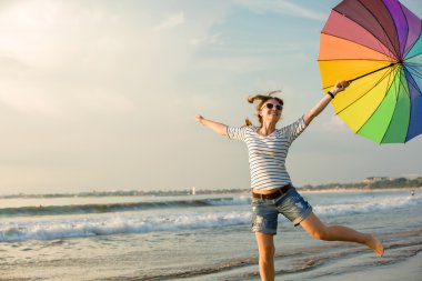 gün batımından önce sahilde eğleniyor gökkuşağı şemsiye ile neşeli genç kız. seyahat, tatil, tatil, sağlıklı yaşam konsepti