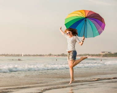 gün batımından önce sahilde eğleniyor gökkuşağı şemsiye ile neşeli genç kız. seyahat, tatil, tatil, sağlıklı yaşam konsepti