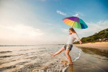 gün batımından önce sahilde eğleniyor gökkuşağı şemsiye ile neşeli genç kız. seyahat, tatil, tatil, sağlıklı yaşam konsepti