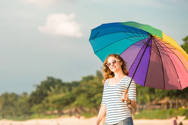 Attractive caucasian woman wearing sunglasses holding colourful rainbow umbrella enjoing beach time before sunset. Travel, holidays, vacation, healthy lifestyle concept — Stock Photo, Image