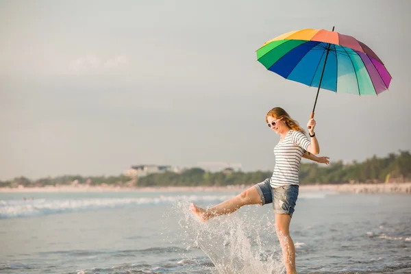 Vidám fiatal lány szivárvány esernyő szórakozás a strandon naplemente előtt. utazás, üdülés, nyaralás, egészséges életmód fogalma — Stock Fotó