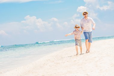 Father with son running barefoot on the sea surf line having great holidays time
