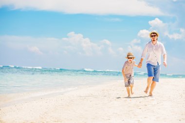 Father with son running barefoot on the sea surf line having great holidays time