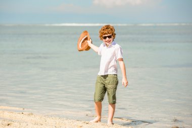 güzel yaz güneşli gün zevk şapka sallayarak hipster güneş gözlüğü takmış kırmızı saçlı çocuk mutlu çocuk sığ suda sahilde kalıyor