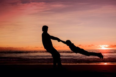 Silhouettes of father spinning his son around on sunset