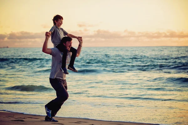 Gelukkig vader en zoon hebben geweldige tijd op het strand bij zonsondergang licht — Stockfoto