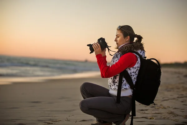 Girl photographer taking pictures with SLR camera at sunset on the beach — 스톡 사진