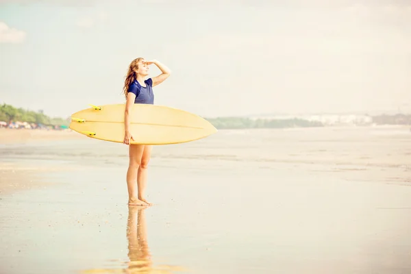 Hermosa chica surfista sexy en la playa al atardecer en busca de olas de la orilla con tabla de surf en sus manos —  Fotos de Stock