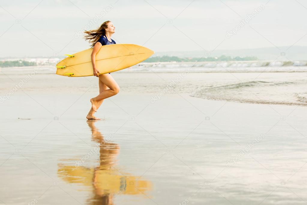 Beautiful sexy surfer girl on the beach at sunset running into ocean, yellow surfboard in her hands. Healthy life, sport  concept with copyspace