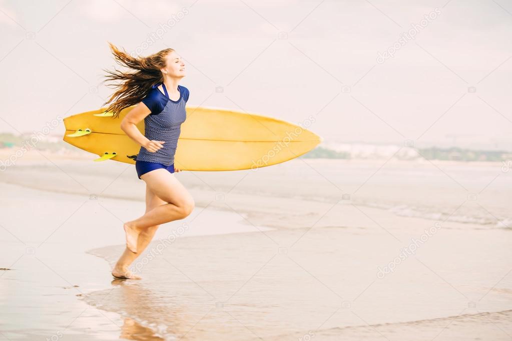 Beautiful sexy surfer girl on the beach at sunset running into ocean, yellow surfboard in her hands. Healthy life, sport  concept with copyspace