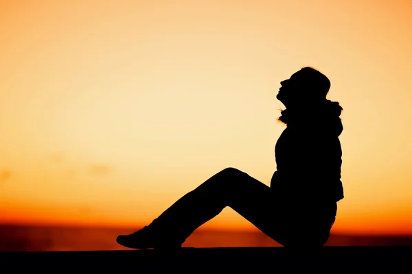 Silhouette of a woman sitting on the edge over beautiful red sunset — Stockfoto