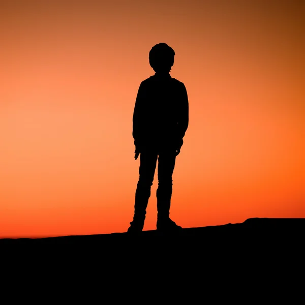 Young boy is standing on pier enjoying the sunset. Silhouette of a kid — Φωτογραφία Αρχείου