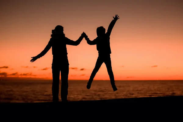Silhouette of young mother having fun with her son, sunset background on summer night — Stok fotoğraf