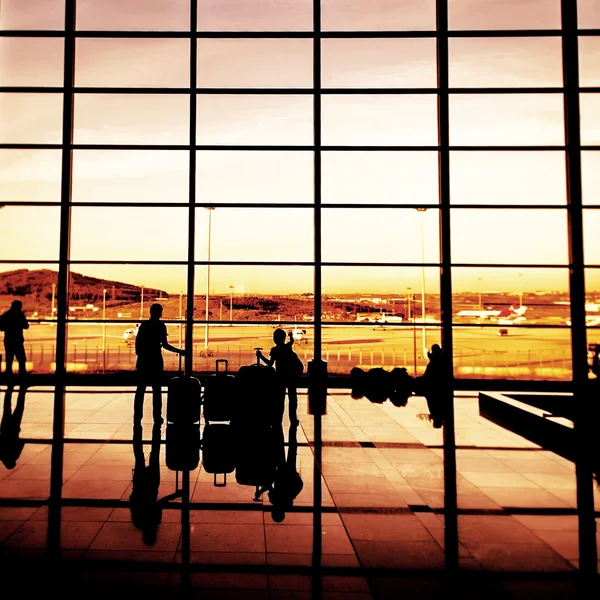 Silhouette dei passeggeri di una compagnia aerea in una lounge dell'aeroporto all'ampia finestra di osservazione contro un tramonto surreale — Foto Stock