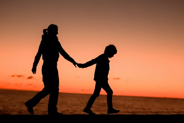 Silhouette of a young mother and her son walking along a pier in front of a sunset in the sky on a summer day — Stock Photo, Image
