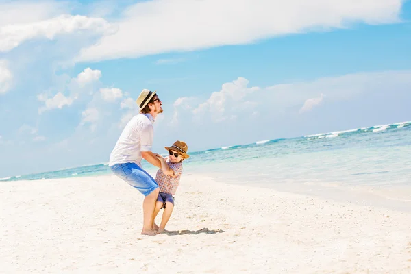 Junger glücklicher Vater spielt mit seinem kleinen Sohn, der barfuß am Strand steht, vor dem Meer und schönen Wolken im Hintergrund — Stockfoto