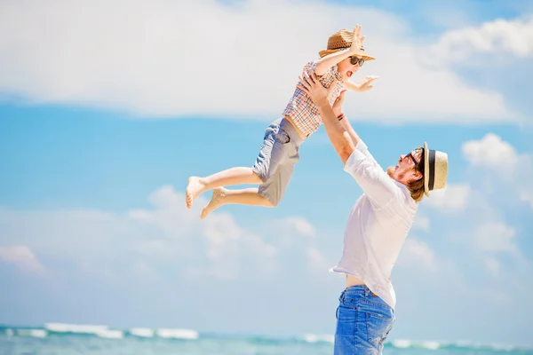 Young happy father playing with his little son standing barefoot at the beach against ocean and beautiful clouds on background — Stock Photo, Image