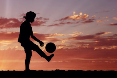 Silhouette of a boy playing football or soccer at the beach with beautiful sunset background