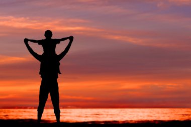 Silhouettes of father and son having fun together in sunset on summer holidays