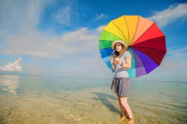 Jovencita alegre con paraguas de arco iris divertirse en la playa —  Fotos de Stock