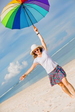 Cheerful young girl with rainbow umbrella having fun on the beach  clipart
