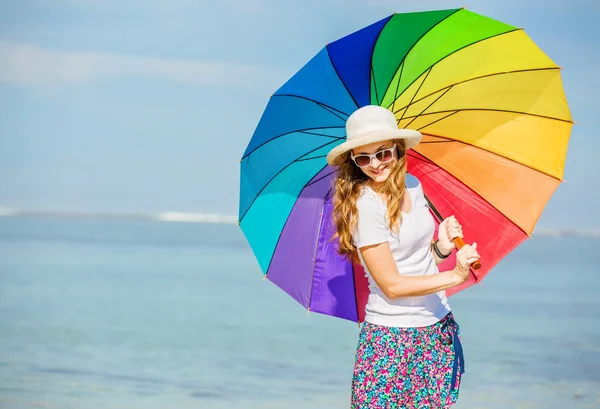 Jovencita alegre con paraguas de arco iris divertirse en la playa — Foto de Stock