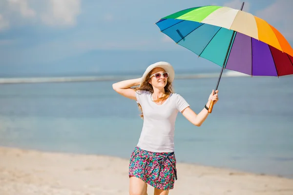 Jovem alegre com guarda-chuva arco-íris se divertindo na praia — Fotografia de Stock