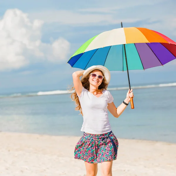 Jovencita alegre con paraguas de arco iris divertirse en la playa — Foto de Stock