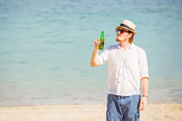 Man wearing hat and sunglasses enjoing beer in a bottle on the beach — Stock Photo, Image