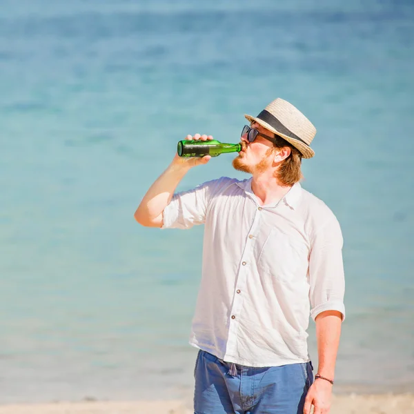 Man wearing hat and sunglasses enjoing beer in a bottle on the beach — Stock Photo, Image