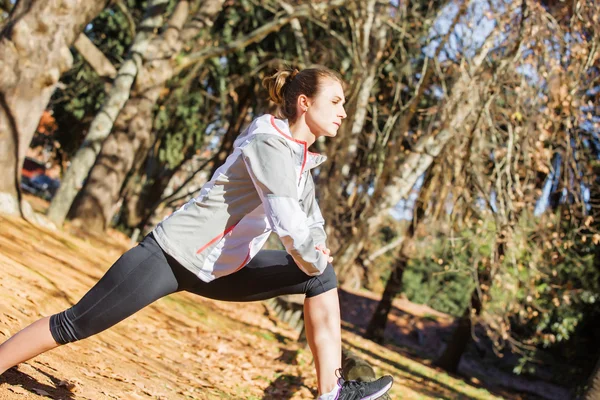 Jeune fille en forme étirant sur le banc avant de faire de l'exercice dans le parc d'automne — Photo