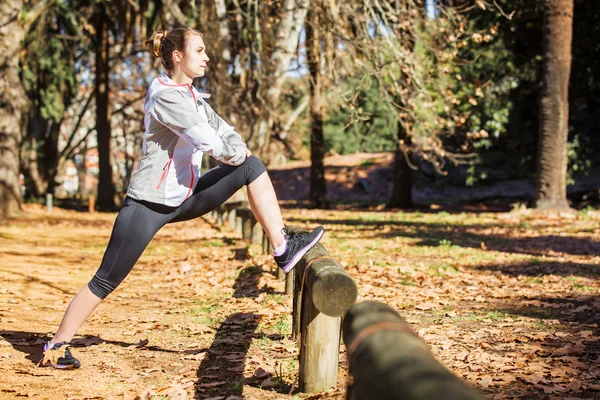 Young fit girl stretching out on bench before exercising in autumn park — Stock Photo, Image