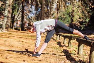 Genç kız bankta sonbahar parkta egzersiz öncesine uzanan yerleştirmek