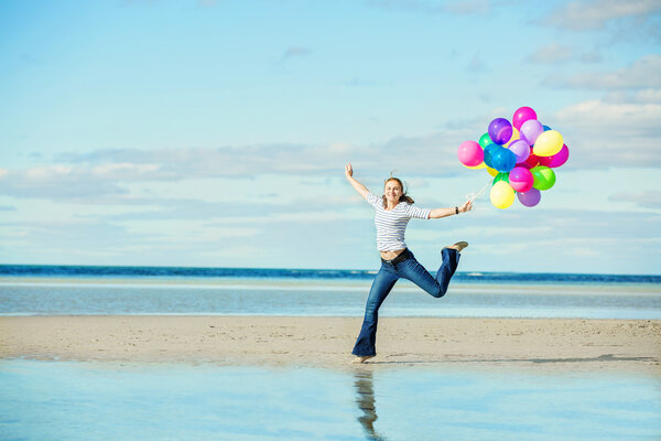 Beautiful girl jumps on the beach while holding colored balloons