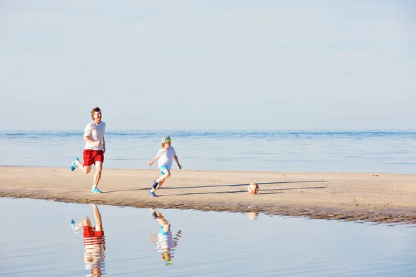 Happy father and son play soccer or football on the beach — Stock Photo, Image