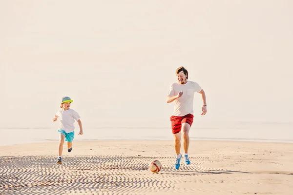 Happy father and son play soccer or football on the beach — Stock Photo, Image