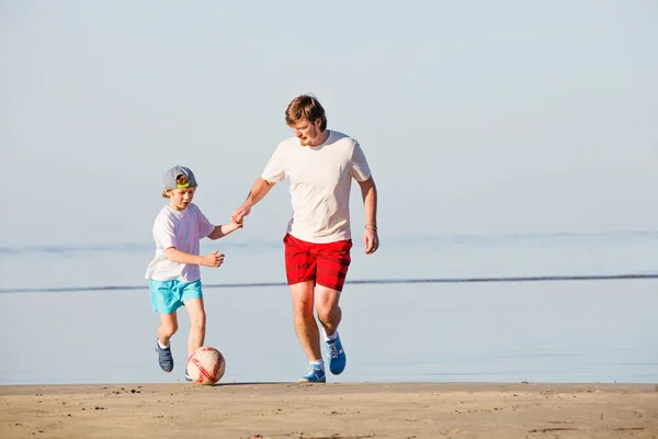 Lycklig far och son spela fotboll eller fotboll på stranden — Stockfoto