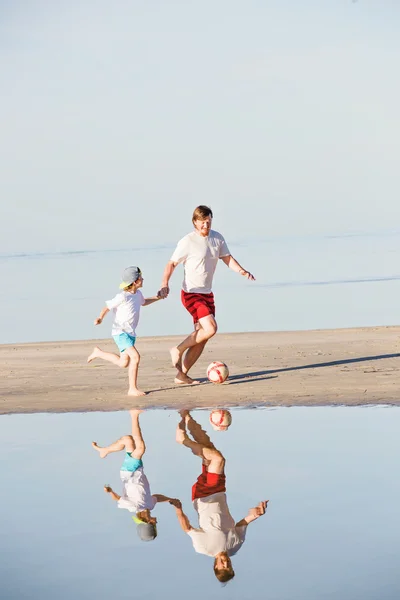 Happy father and son play soccer or football on the beach — Stock Photo, Image