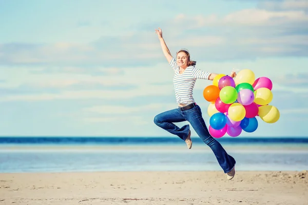 Piękna dziewczyna skacze na plaży trzymając kolorowe balony — Zdjęcie stockowe