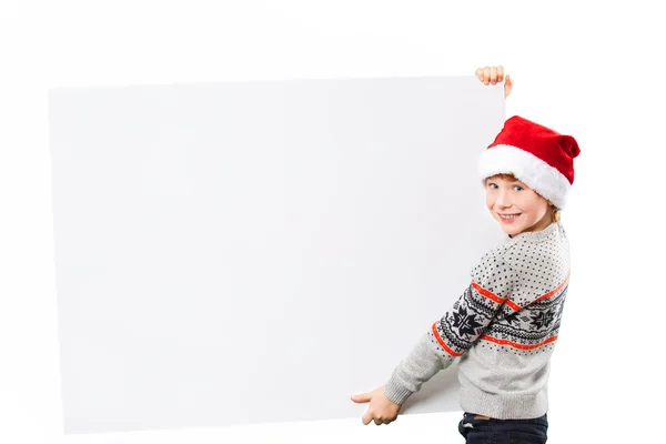 Portrait of a boy in christmas hat holding white blank. Isolated — Stock Photo, Image